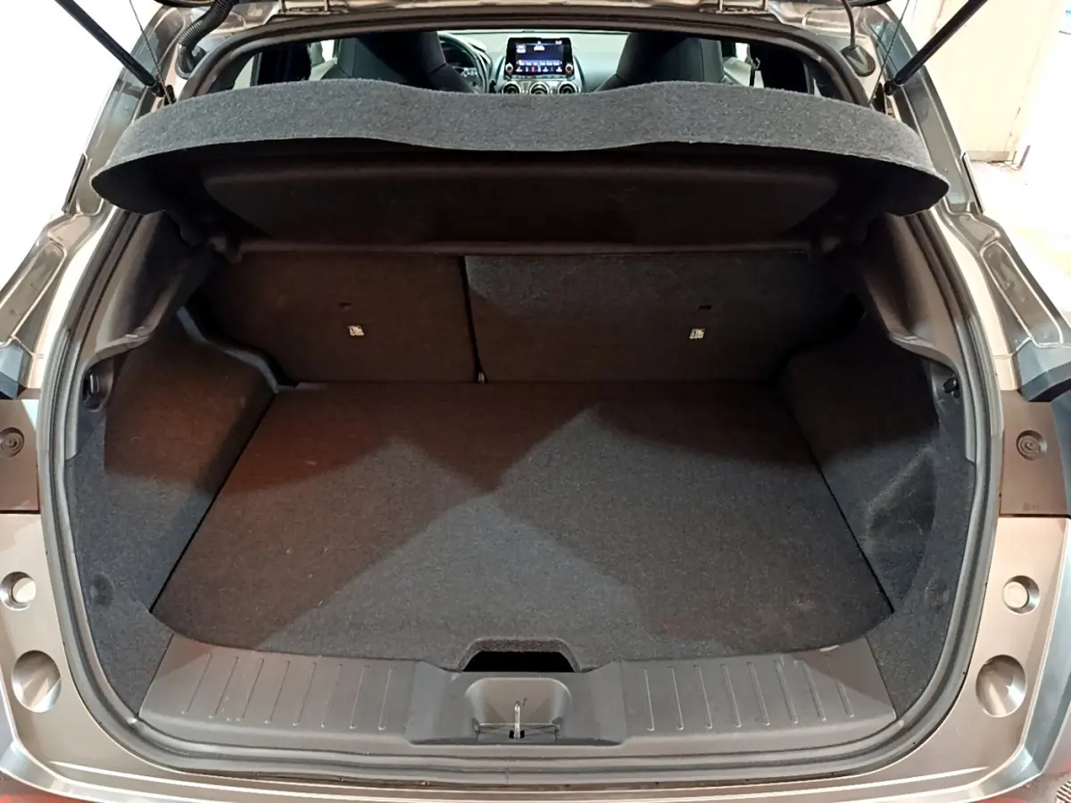 Coffre ouvert vu de l'arrière d'un Nissan Juke Hybrid 143 Business+ gris foncé, intérieur noir et tablette de coffre visible.