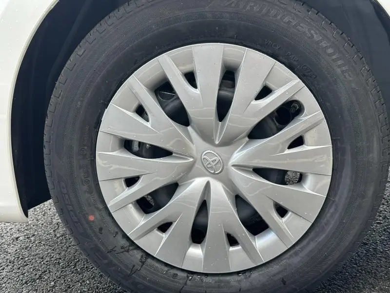 Gros plan sur la roue avant gauche d'une Toyota Yaris 116h Dynamic blanche, avec enjoliveur argenté et logo Toyota central.