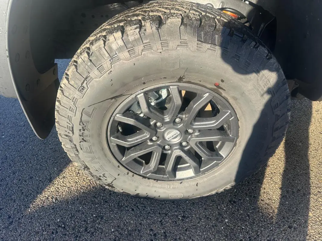 Gros plan sur la roue avant droite du Ford Ranger blanc, jante alliage noire avec pneu tout-terrain.