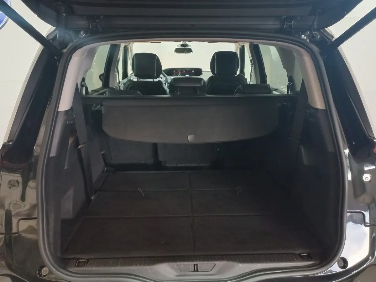 Coffre ouvert vu de l'arrière d'un Citroën Grand C4 Spacetourer noir avec banquette arrière rabattue et cache-bagages déployé.