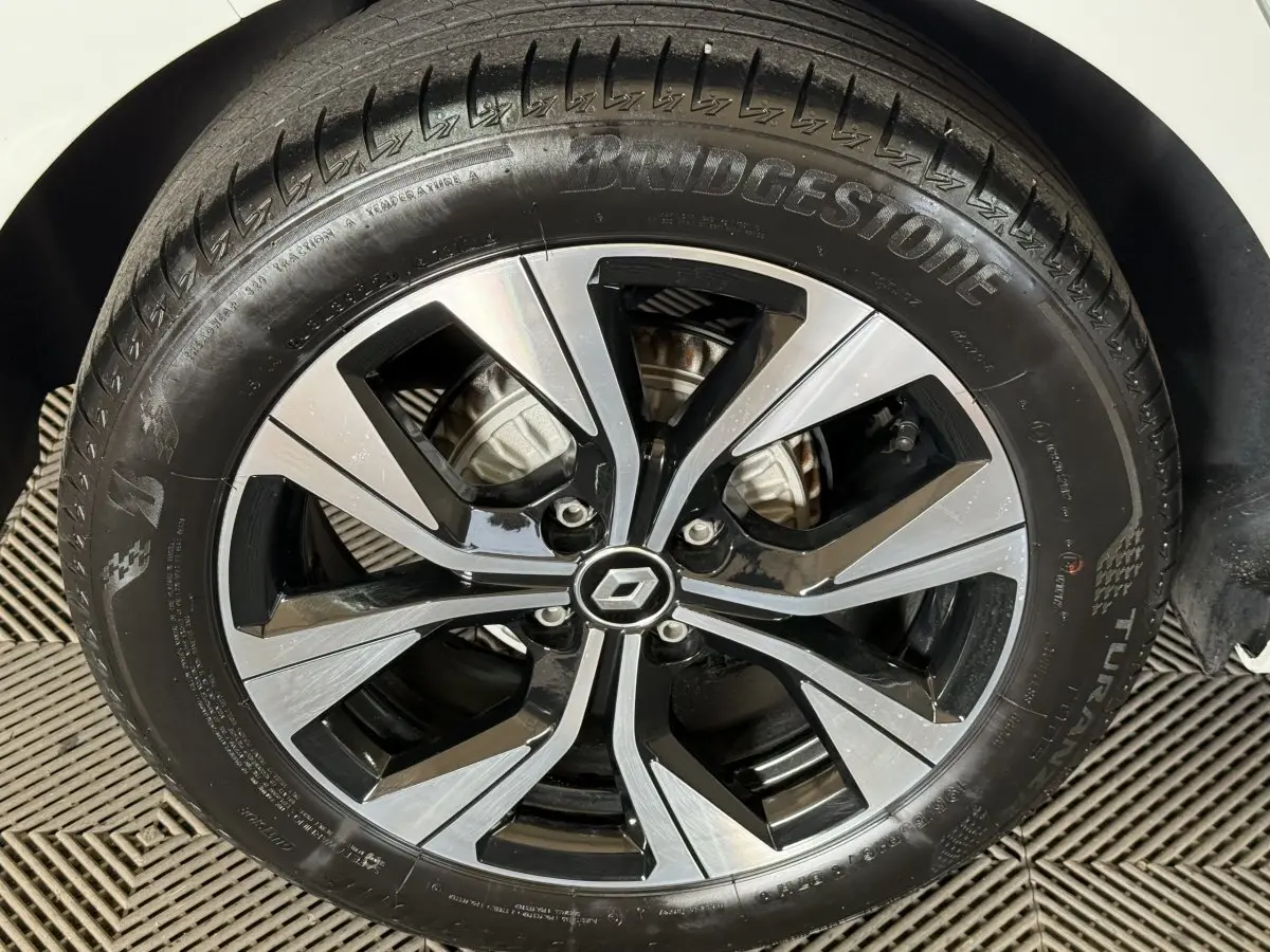 Gros plan sur la jante alliage bicolore noir et argent avec logo Renault au centre, pneu Bridgestone monté sur Clio blanche.