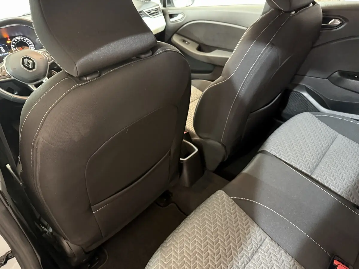 Vue intérieure arrière droite de la Renault Clio Business blanche, sièges tissu gris et noir avec surpiqûres blanches.