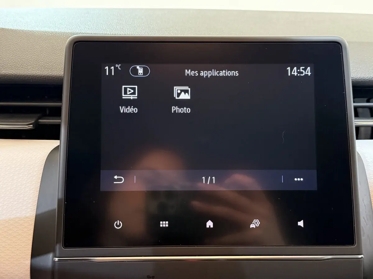 Écran tactile central de la Renault Clio Business blanc, affichant le menu des applications avec température et heure.