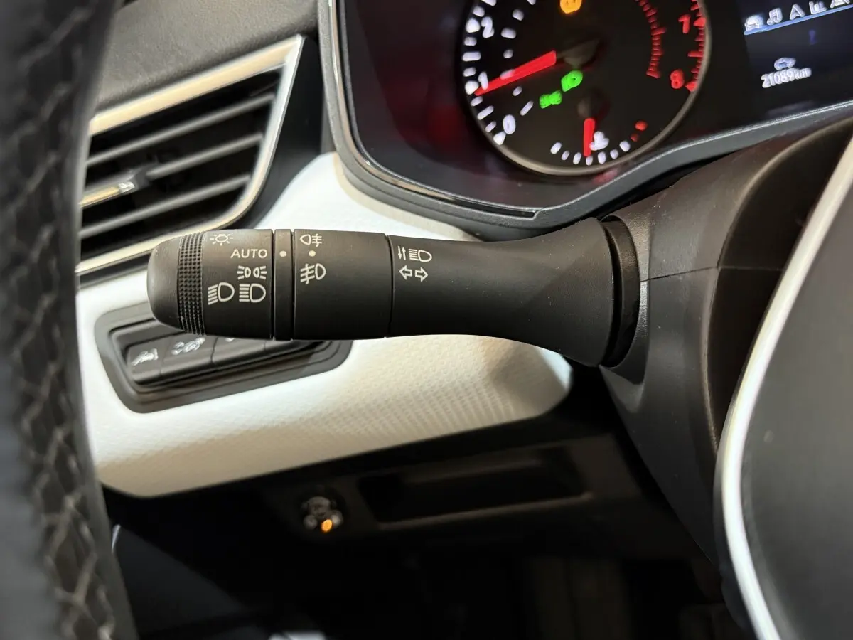 Gros plan sur la manette des phares et clignotants à gauche du volant dans l’habitacle blanc et noir d’une Renault Clio Business 2022.