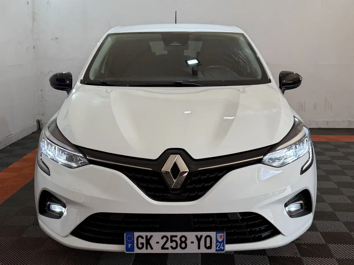 Vue frontale d'une Renault Clio Business blanche avec feux LED allumés et calandre noire brillante.