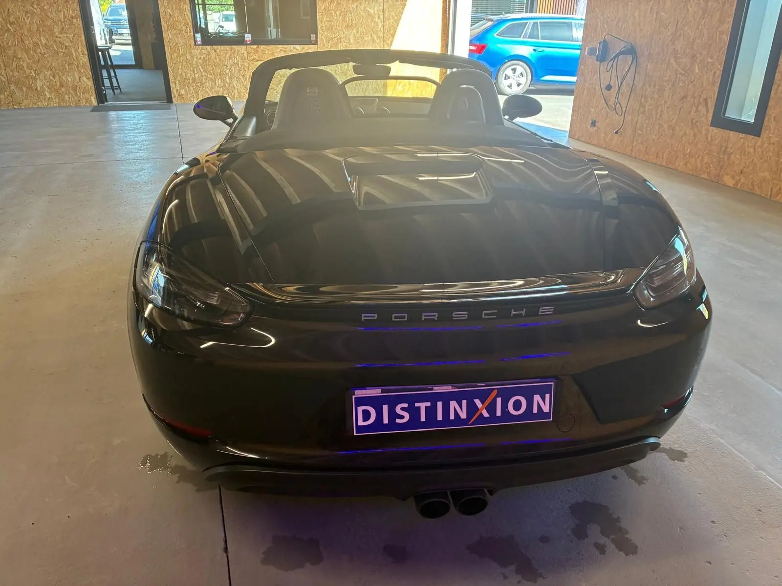 Vue arrière d'une Porsche 718 Boxster noire cabriolet, avec capote baissée et double sortie d'échappement centrale.