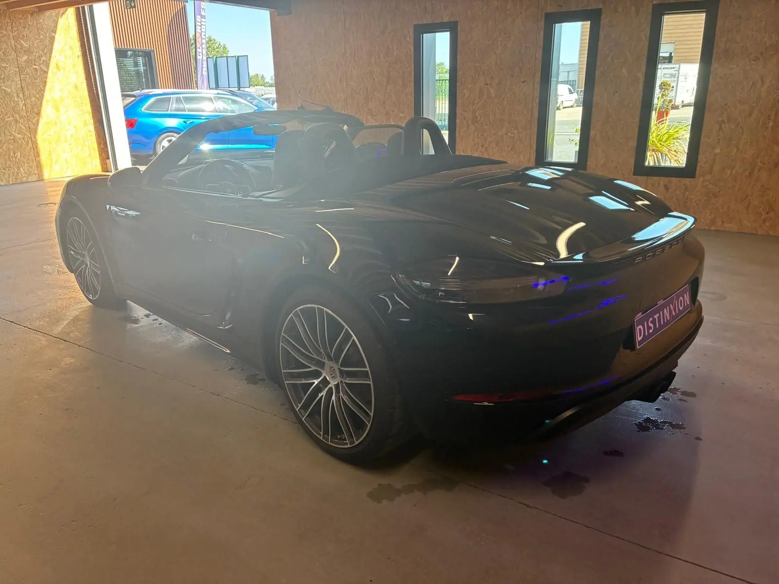 Vue 3/4 arrière droite d'une Porsche 718 Boxster noire cabriolet, avec jantes alliage et intérieur visible en alcantara noir.
