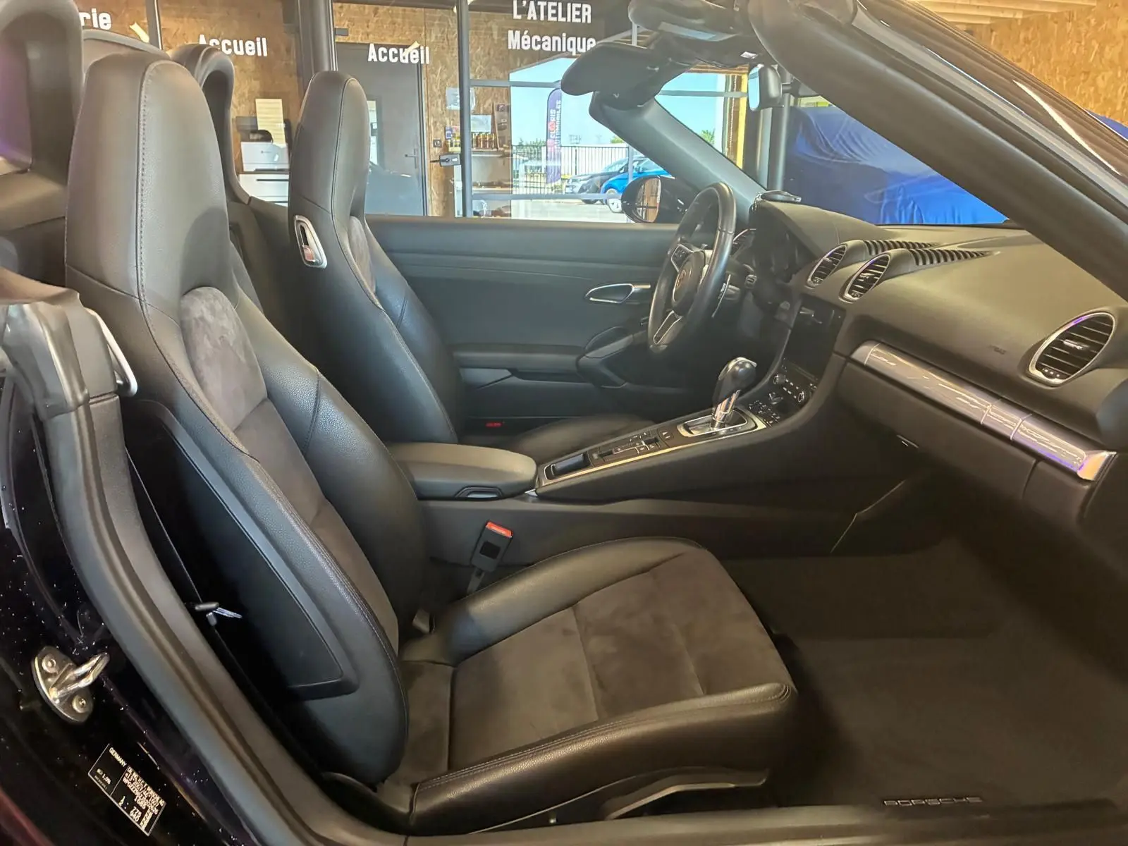 Vue intérieure côté gauche de la Porsche 718 Boxster noire, mettant en valeur les sièges sport en cuir et alcantara et la console centrale.