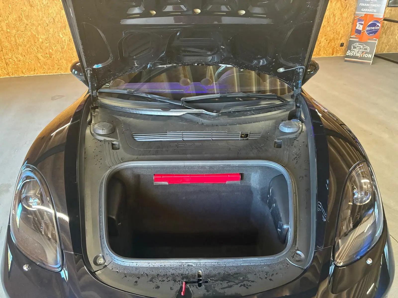 Vue plongeante avant du coffre ouvert d'une Porsche 718 Boxster noire, mettant en valeur l'espace de rangement avant.
