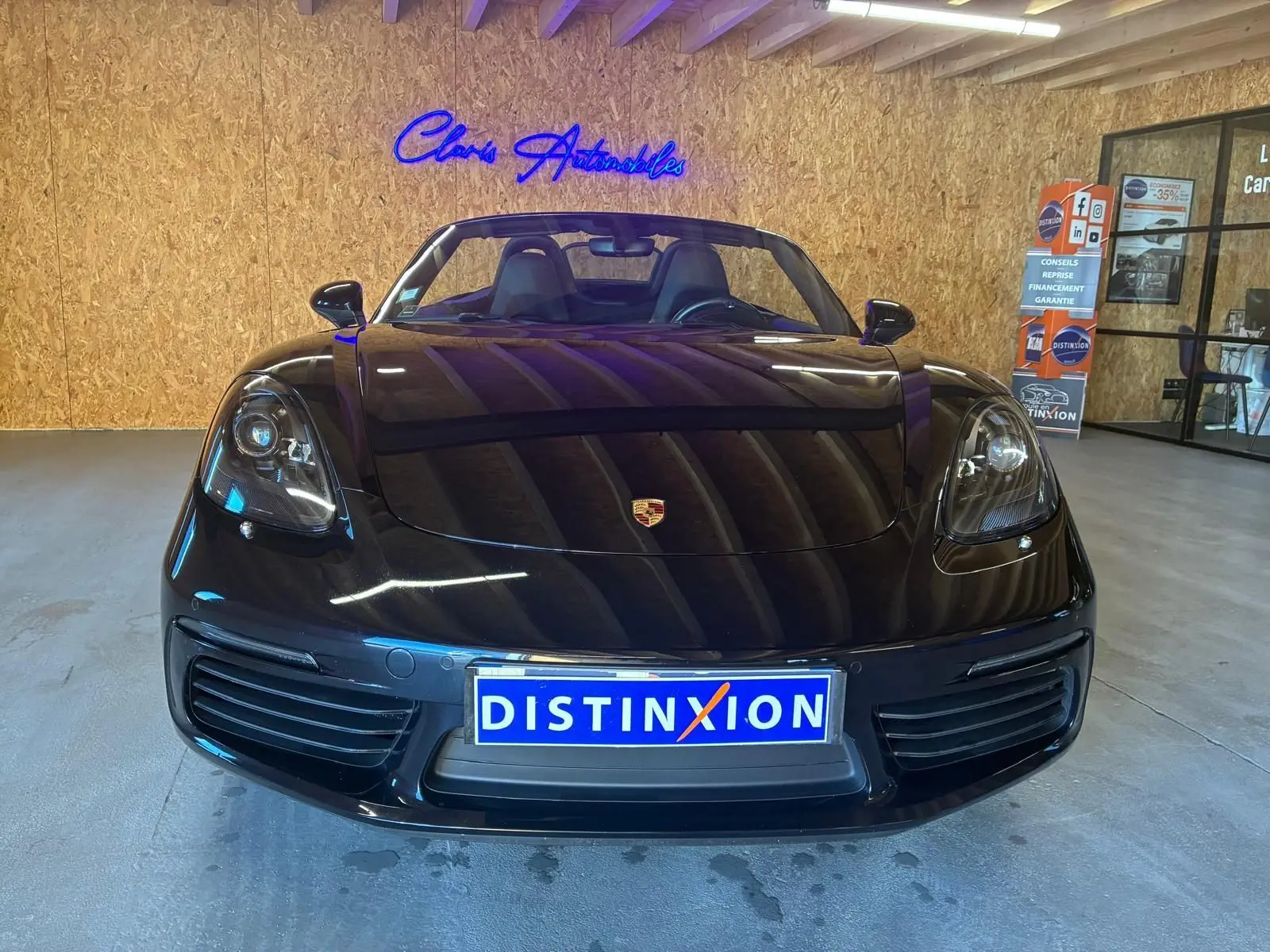 Vue frontale d'une Porsche 718 Boxster noire 2018, capote ouverte, avec logo Porsche visible sur le capot.
