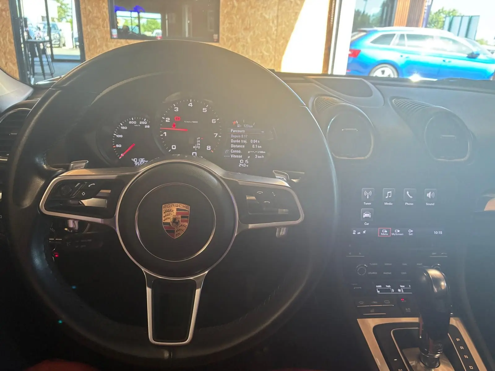 Vue intérieure centrée sur le volant noir de la Porsche 718 Boxster 2.0 300 de 2018 avec tableau de bord et console centrale visibles.
