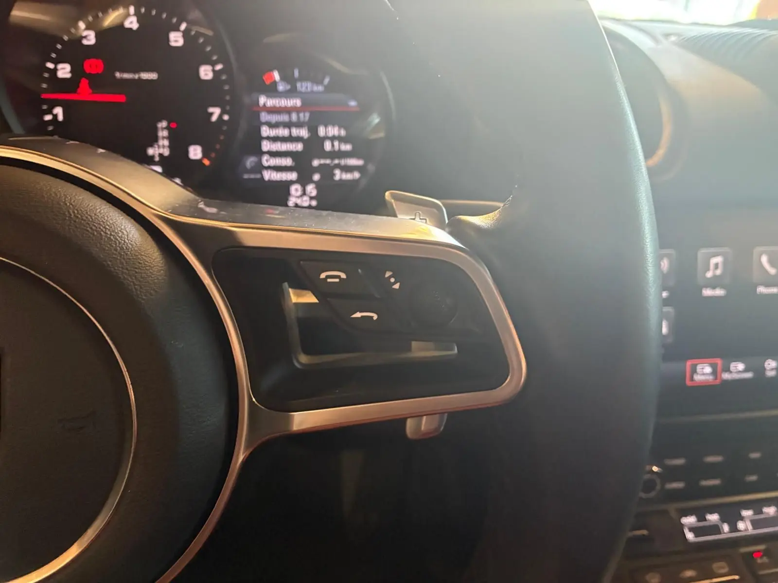 Vue rapprochée du côté gauche du volant noir de la Porsche 718 Boxster 2018 avec commandes intégrées et tableau de bord lumineux.