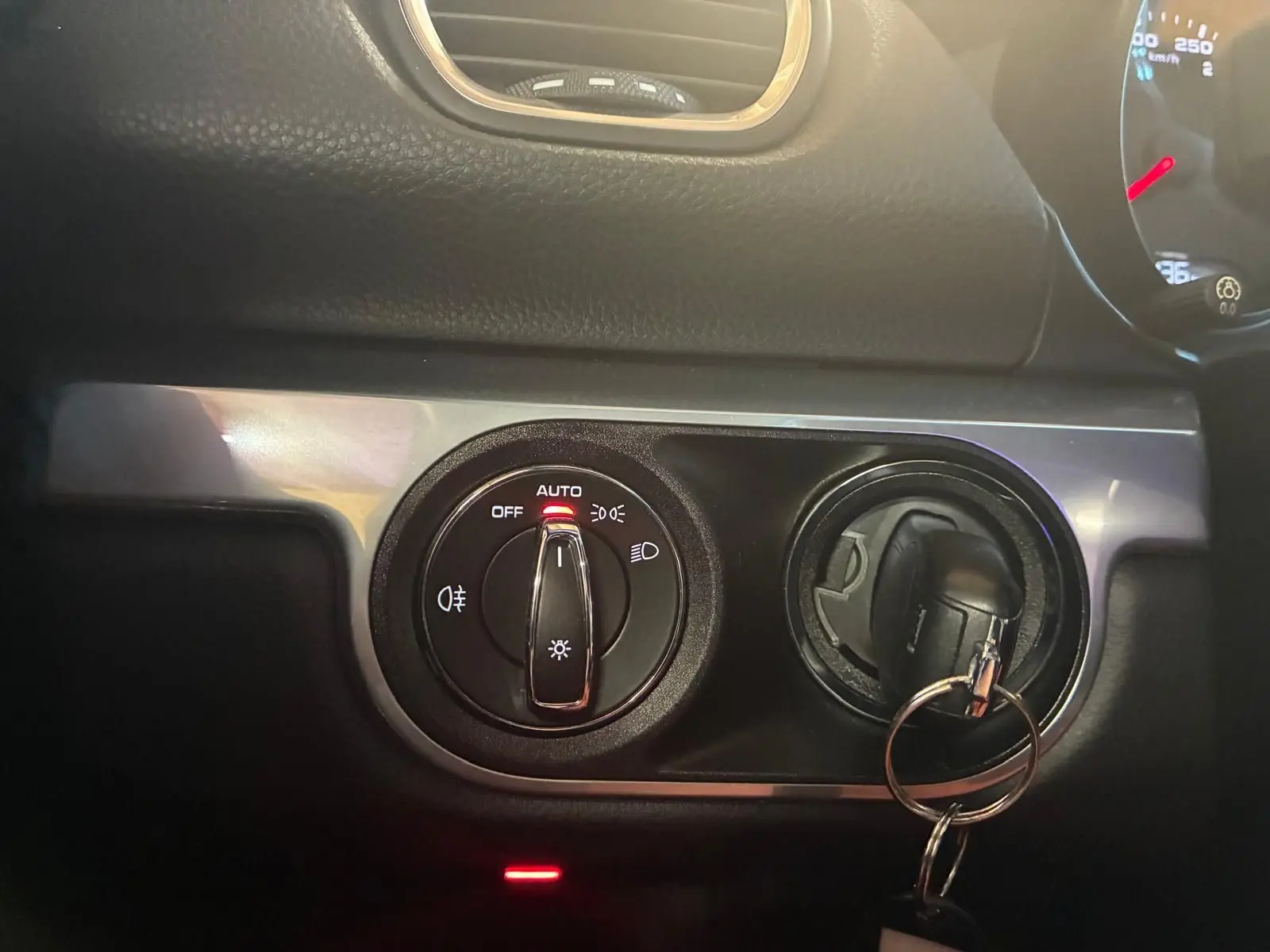 Détail du tableau de bord noir de la Porsche 718 Boxster 2.0 300 de 2018, avec commande des phares en position auto et clé insérée.