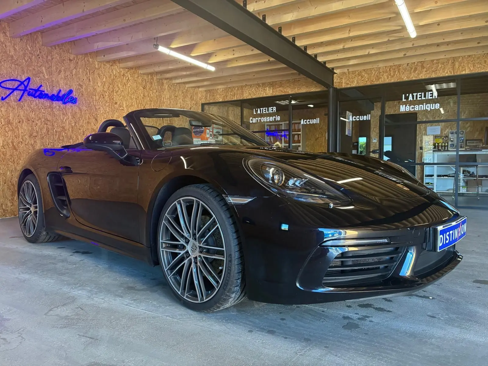 Vue 3/4 avant droite d'une Porsche 718 Boxster 2.0 300 noire cabriolet, avec jantes alliage et intérieur visible.
