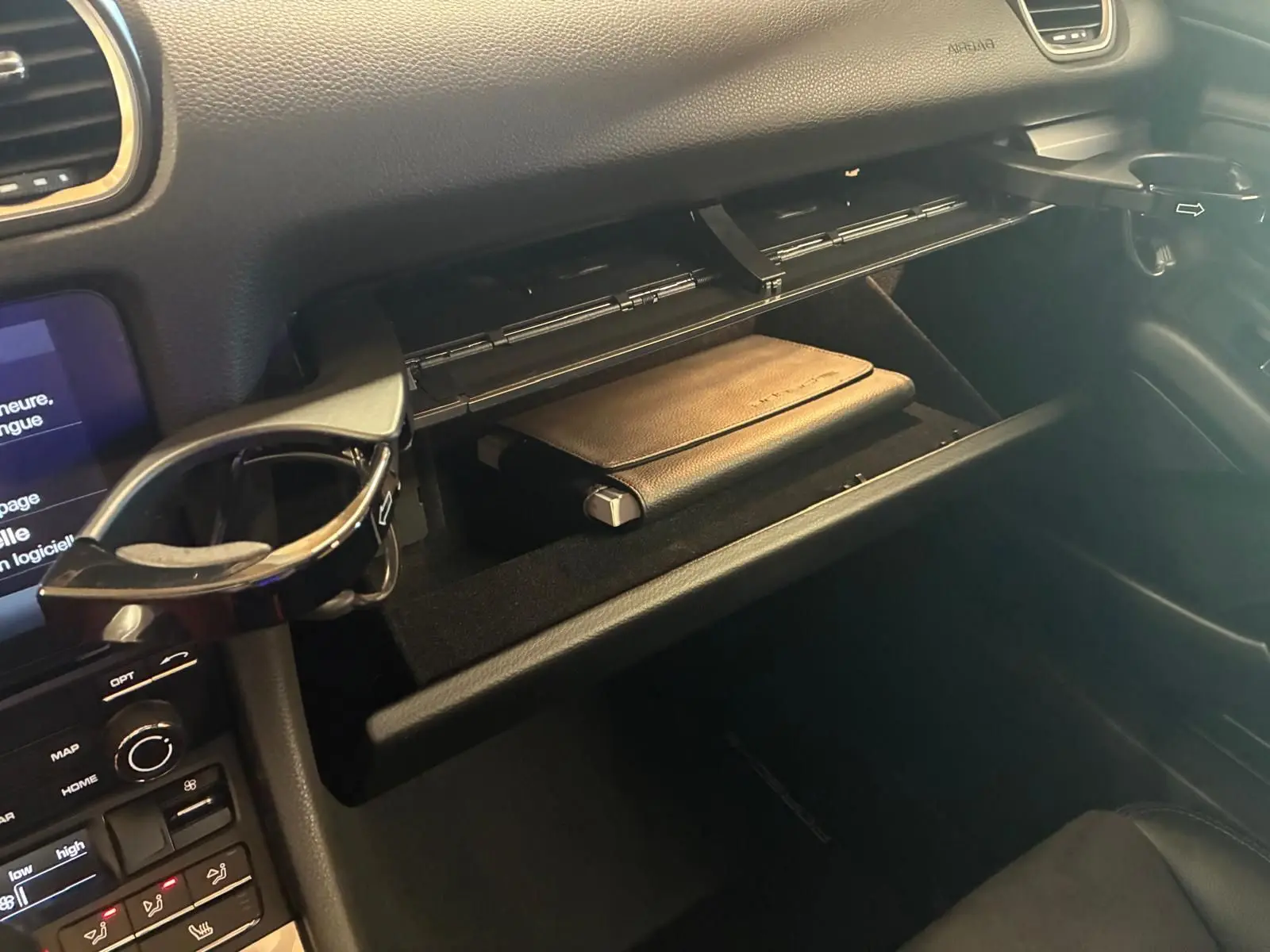 Vue intérieure côté passager du coffre à gants ouvert d'une Porsche 718 Boxster noire avec un porte-gobelet déployé.