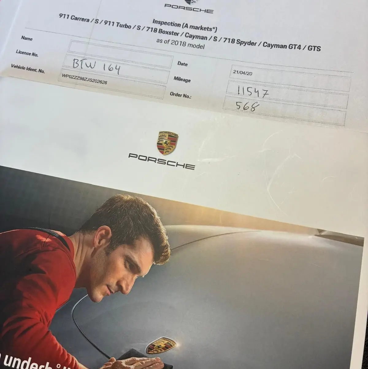 Homme en train de polir le capot avant noir d'une Porsche 718 Boxster 2.0 300 vue de face, mettant en valeur l'écusson Porsche.