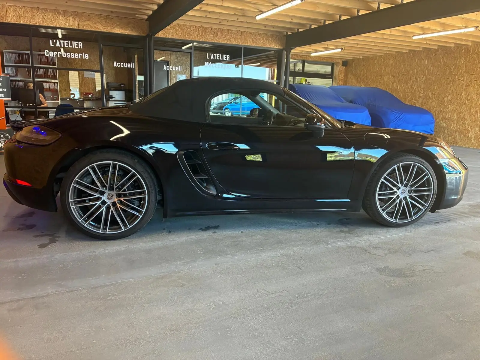 Vue latérale gauche d'une Porsche 718 Boxster noire de 2018 avec toit souple et jantes alliage multibranches.