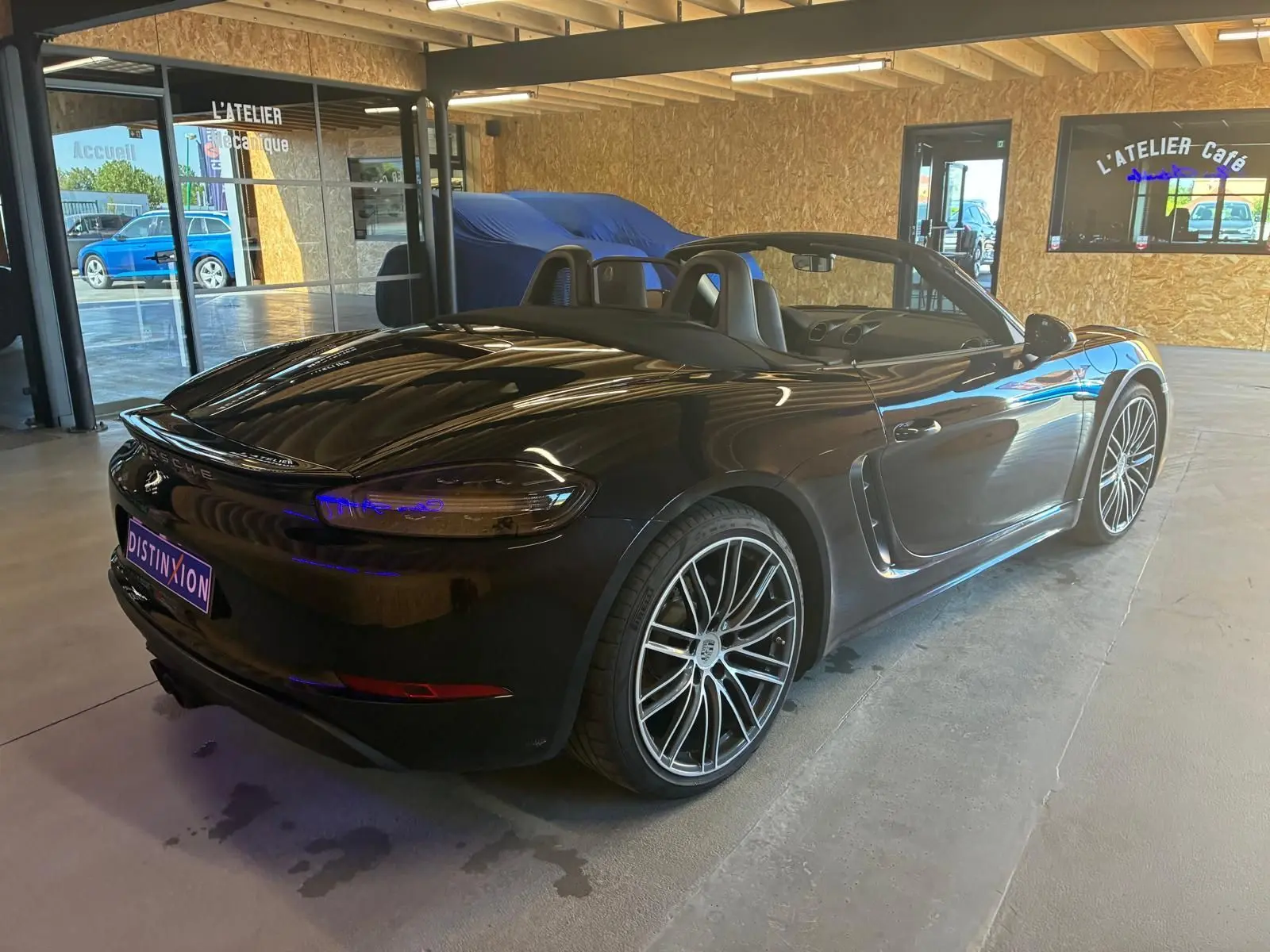 Vue 3/4 arrière droite d'une Porsche 718 Boxster noire cabriolet avec jantes alliage et intérieur ouvert.
