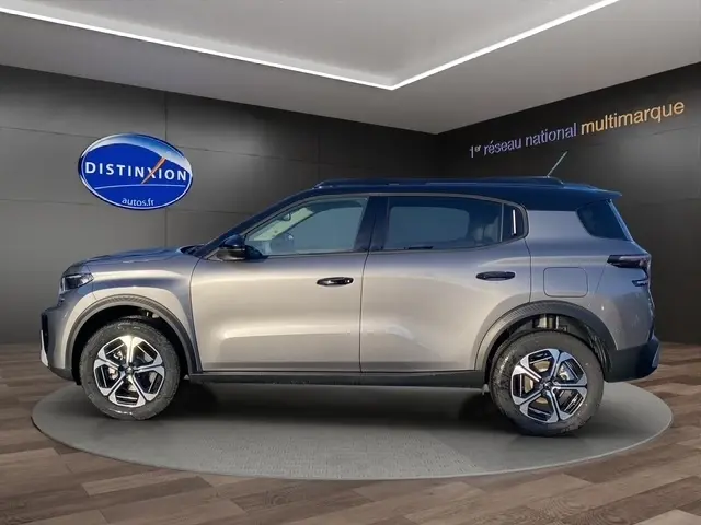 Vue latérale droite d'un Citroën C3 Aircross gris foncé avec toit noir, jantes alliage et barres de toit noires en showroom.