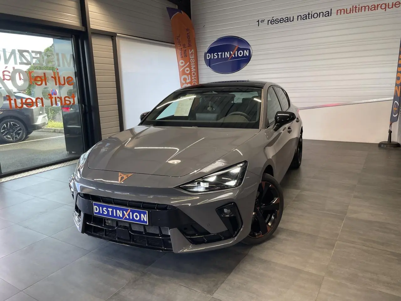 Vue 3/4 avant d'une CUPRA Leon gris Graphène avec jantes cuivrées et logo CUPRA sur le capot, en showroom.