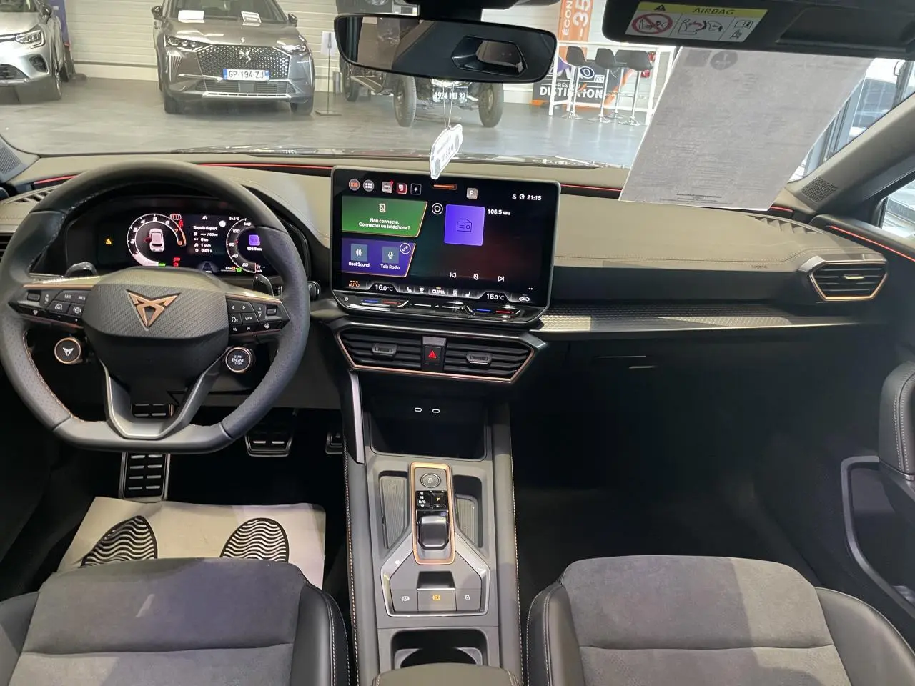 Vue intérieure avant de la CUPRA Leon 1.5 eTSI Hybrid 2026, tableau de bord noir avec écran tactile et volant cuir au logo cuivré.