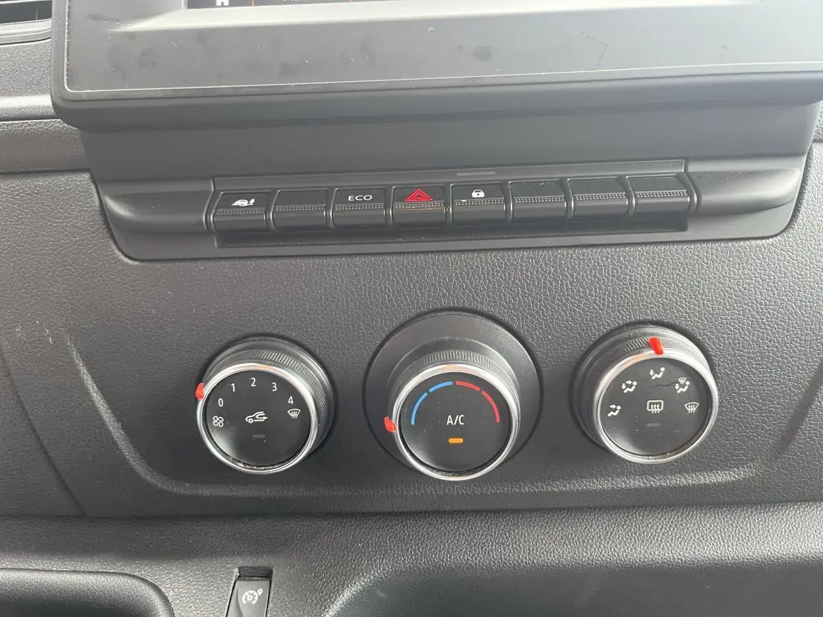 Commandes de climatisation manuelle avec trois molettes et boutons de fonction sur tableau de bord noir du Renault Master blanc 2023.