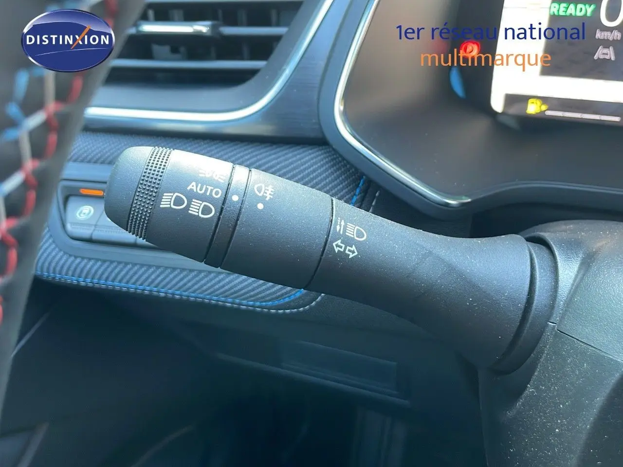 Gros plan sur la commande des feux et clignotants du Renault Captur E-Tech hybride 2025, intérieur noir avec surpiqûres bleues.