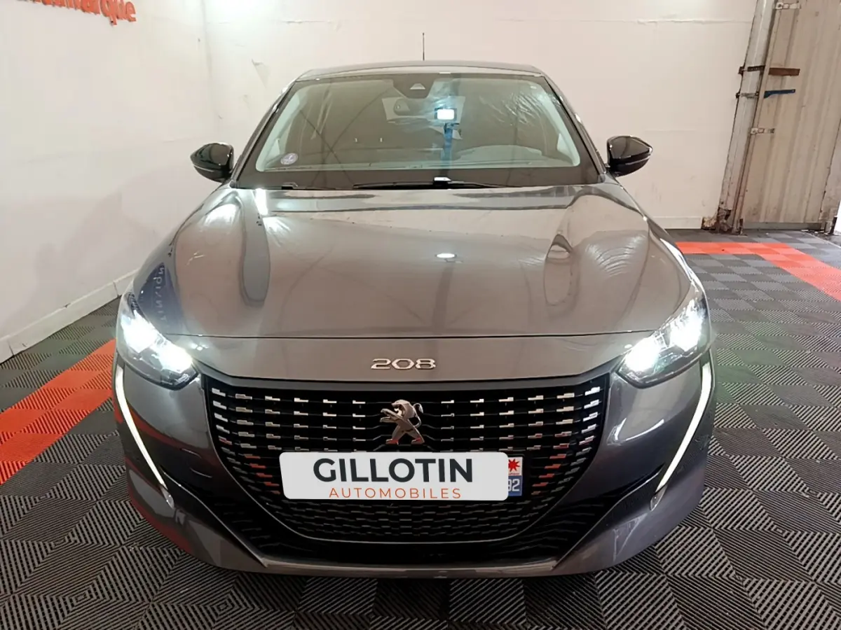 Vue frontale d'une Peugeot 208 gris foncé avec phares LED allumés et calandre noire distinctive.