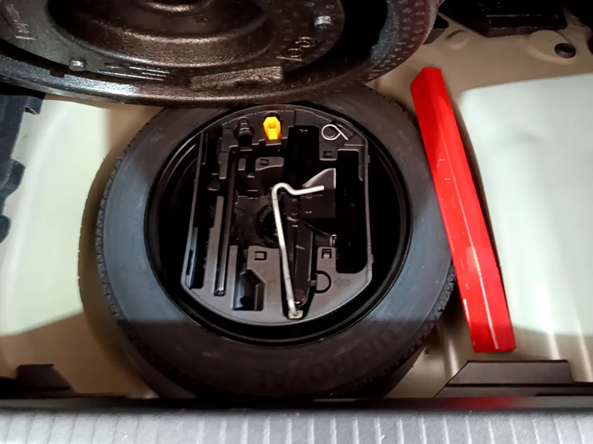 Vue plongeante sur la roue de secours et le kit d'outils dans le coffre d'une Peugeot 208 gris foncé 2022.