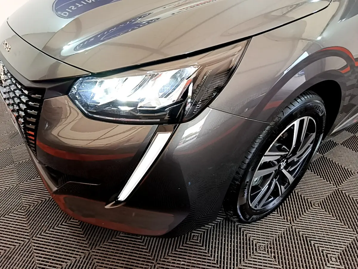 Gros plan sur l'avant droit d'une Peugeot 208 gris foncé 2022, mettant en valeur le phare LED et la jante alliage.