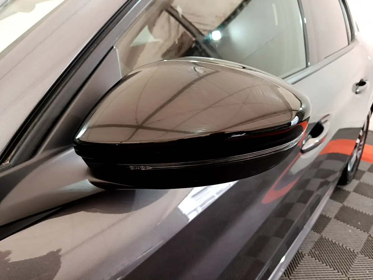Rétroviseur noir côté gauche d'une Peugeot 208 gris foncé, vue rapprochée sur la portière avant.