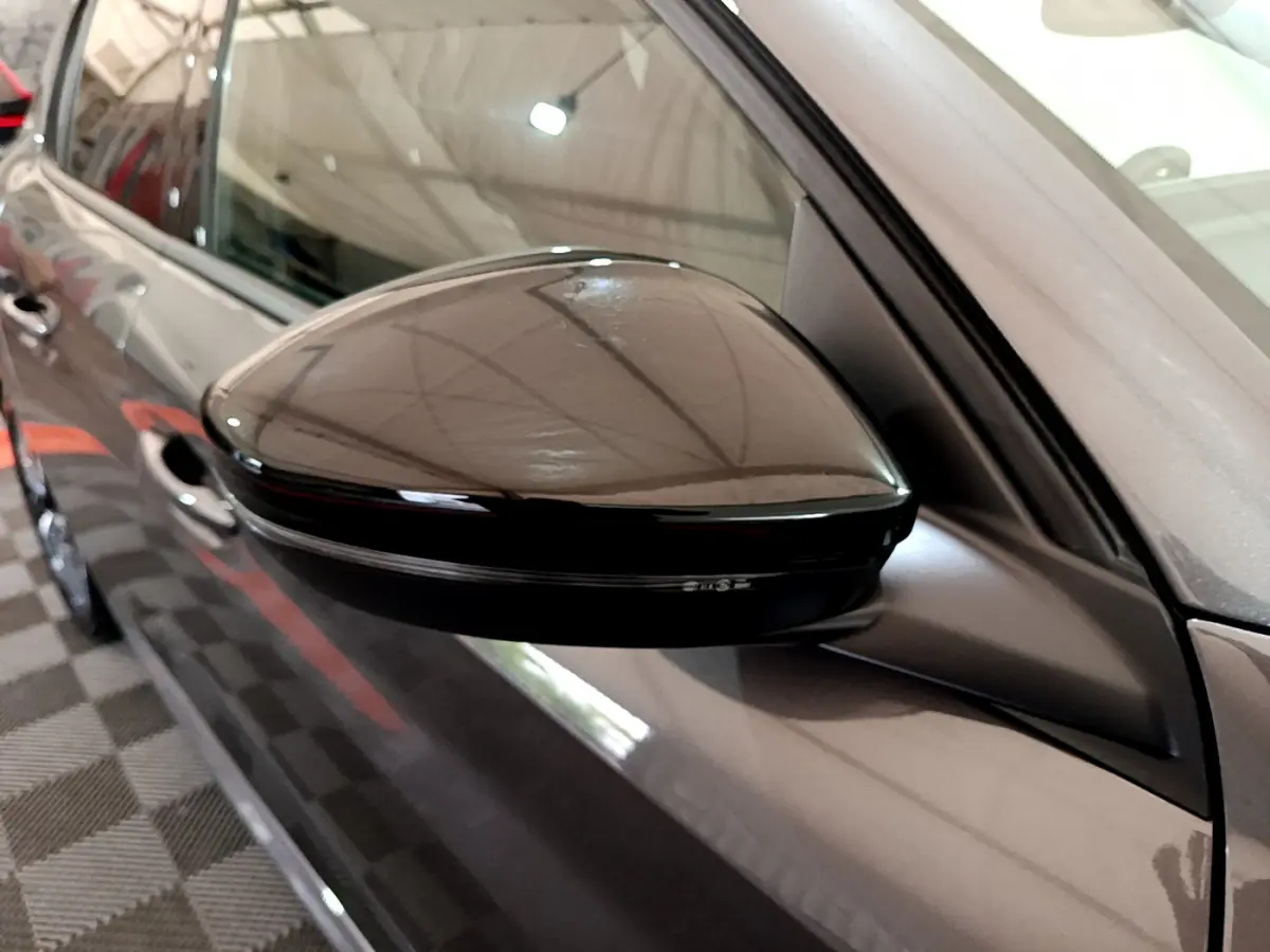 Rétroviseur côté gauche noir brillant d’une Peugeot 208 gris foncé vue en gros plan intérieur garage.