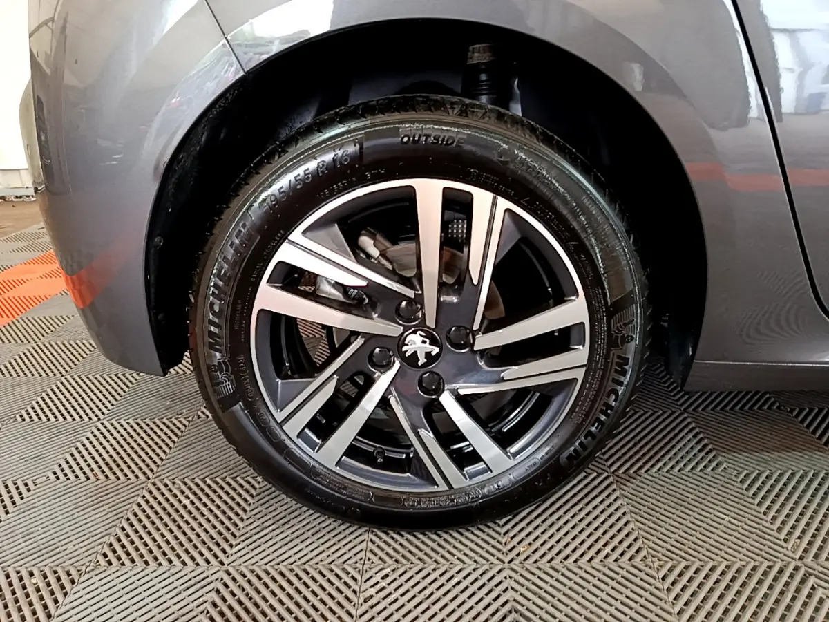 Gros plan sur la roue avant gauche gris foncé d'une Peugeot 208 avec jante alliage et logo lion central.