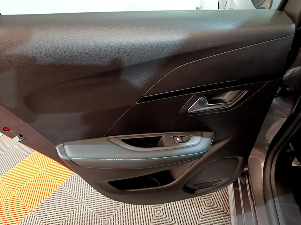 Vue intérieure de la porte avant droite gris foncé de la Peugeot 208 PureTech 100 Allure Pack avec surpiqûres bleues.