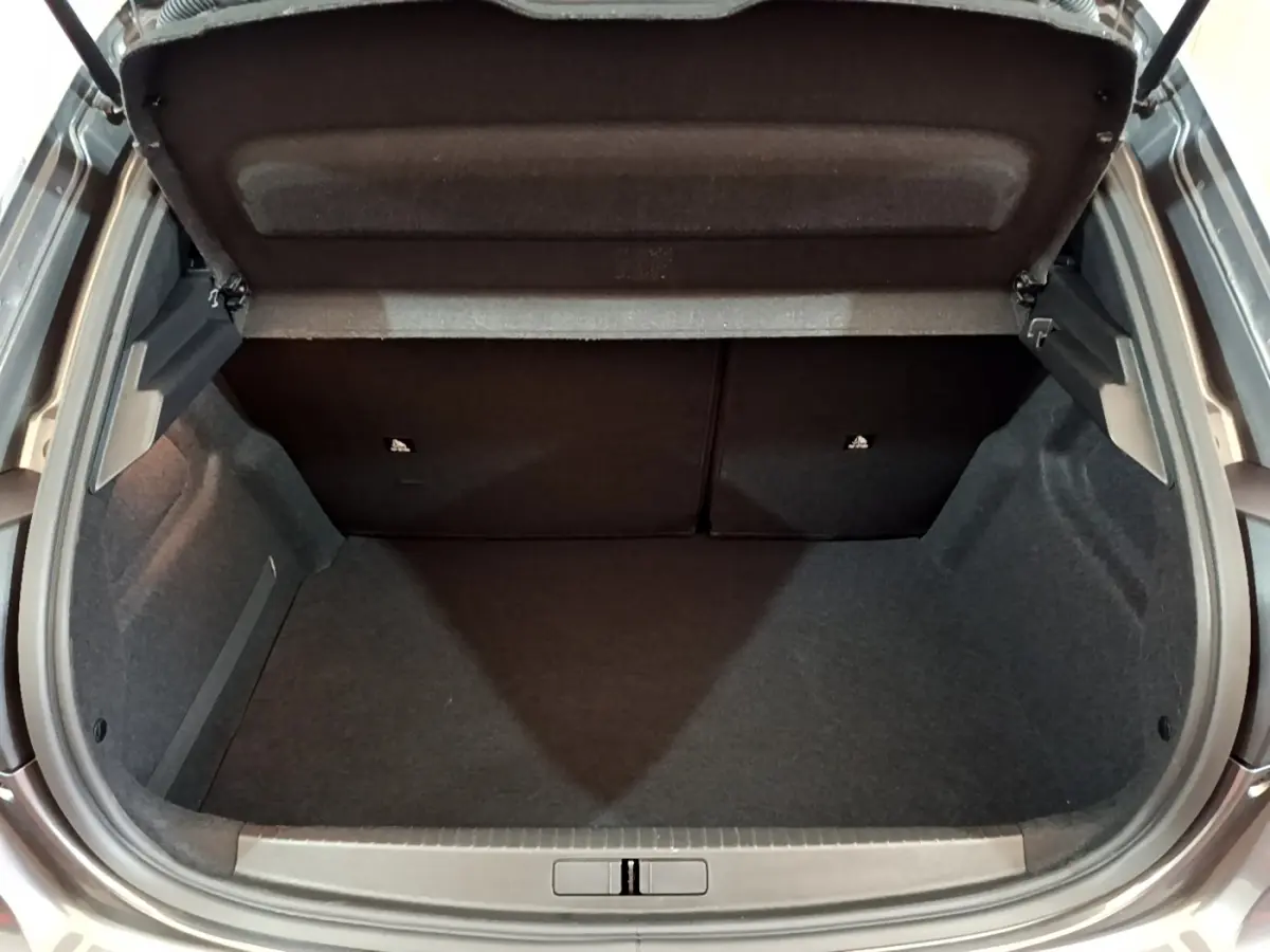 Coffre ouvert vu de l'arrière d'une Peugeot 208 gris foncé, montrant l'espace de chargement vide et les sièges rabattables.