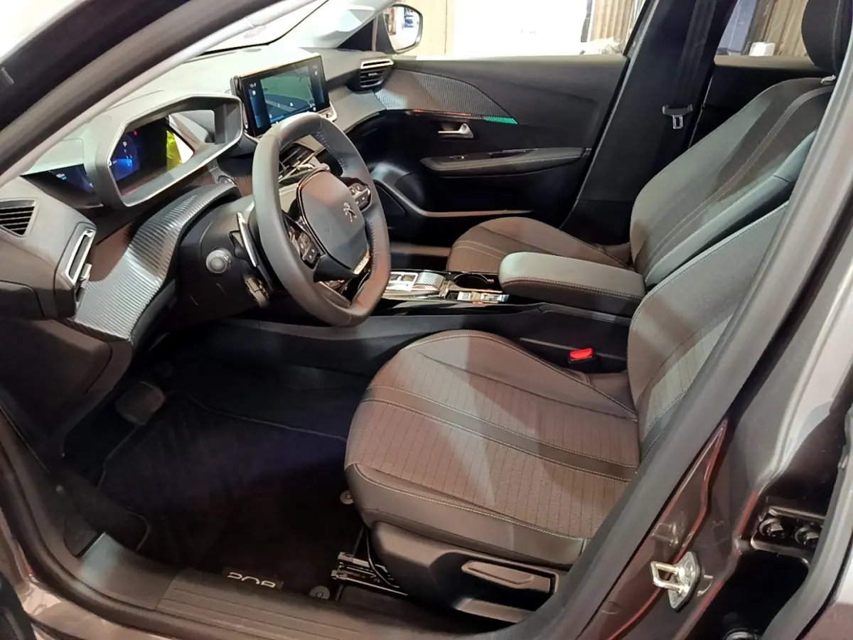 Intérieur avant droit du Peugeot 208 gris foncé 2022, volant cuir, écran tactile et sièges tissu gris.