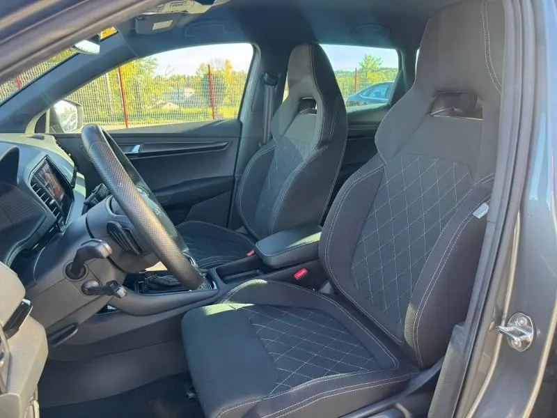 Intérieur vu côté conducteur du Skoda Karoq gris, sièges sport noirs avec surpiqûres et volant cuir multifonction.