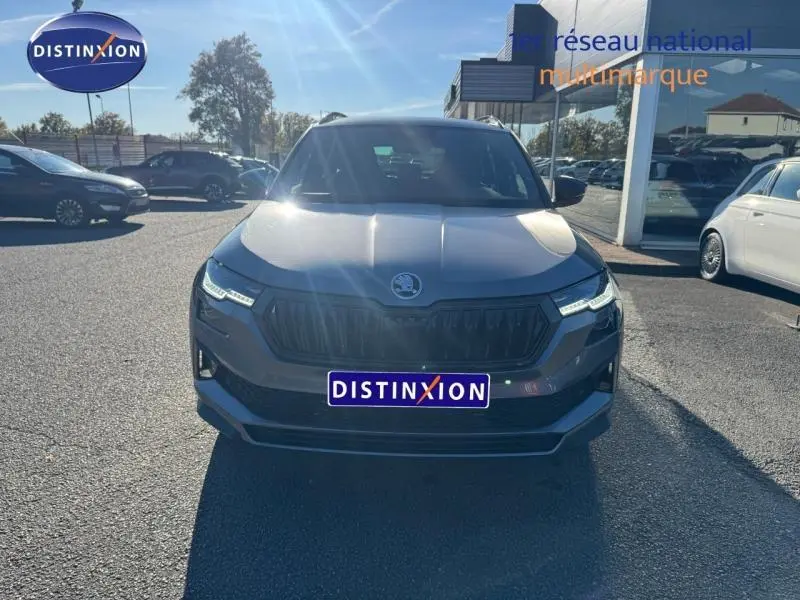 Vue avant d'un SKODA KAROQ gris perle avec calandre noire et phares LED, stationné en extérieur au soleil.