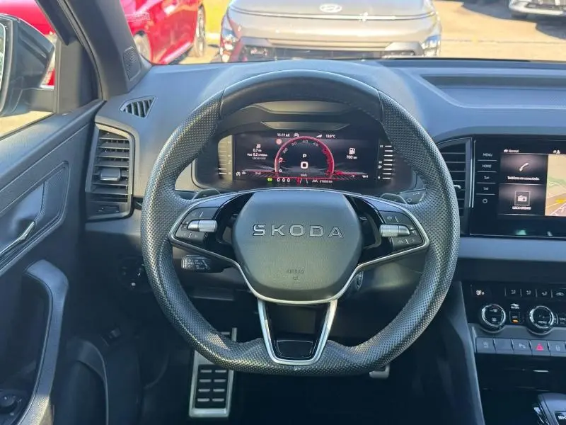 Vue intérieure centrée sur le volant cuir perforé SKODA du Karoq 2025 avec tableau de bord numérique et écran tactile latéral.