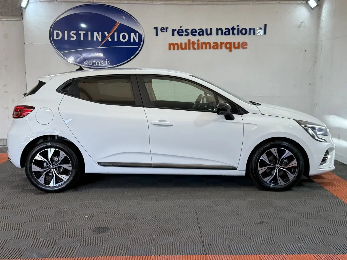 Profil droit d'une Renault Clio Business TCe 100 GPL blanche, avec jantes alliage et rétroviseurs noirs, en intérieur showroom.