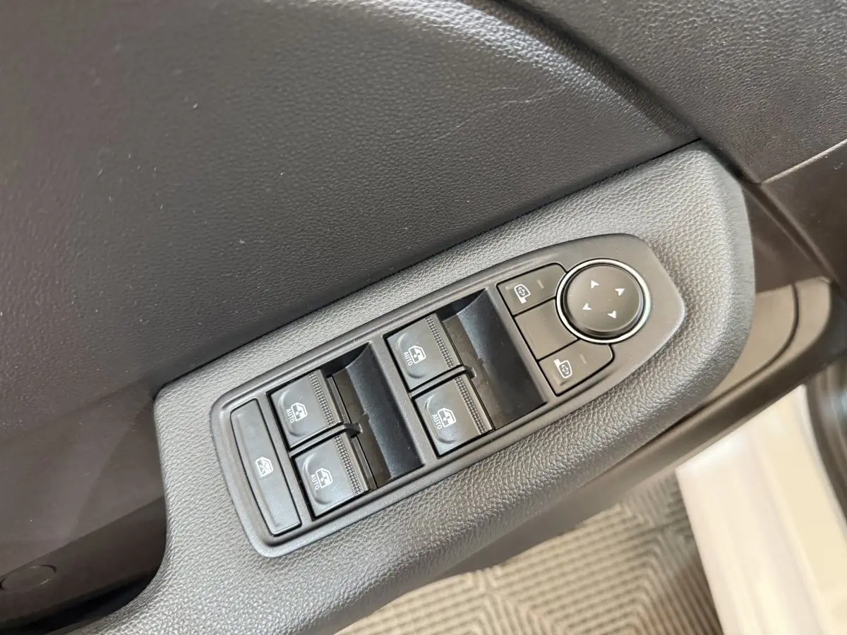 Gros plan sur les commandes des vitres électriques et rétroviseurs sur la porte côté gauche d'une Renault Clio blanche.