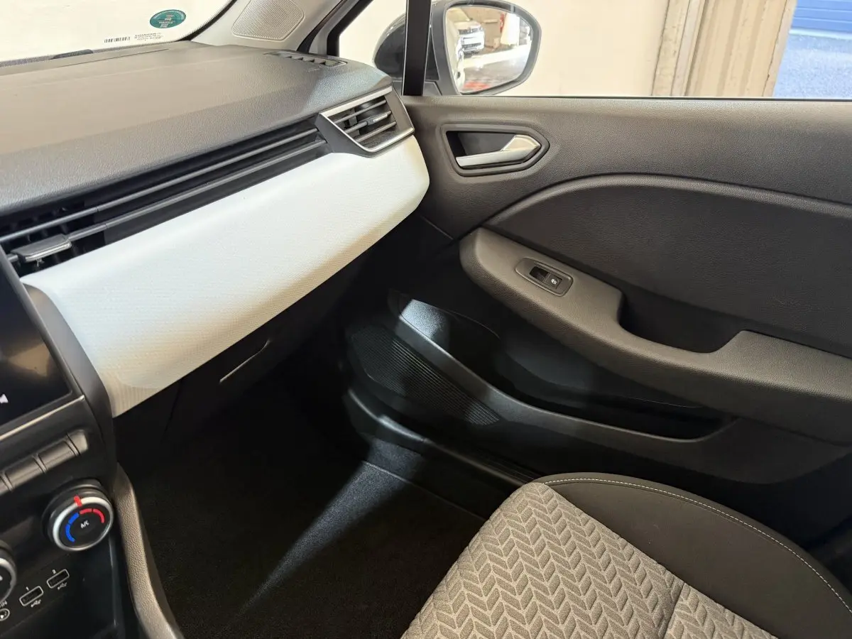 Intérieur côté passager de la Renault Clio Business blanc, avec tableau de bord clair et porte noire.