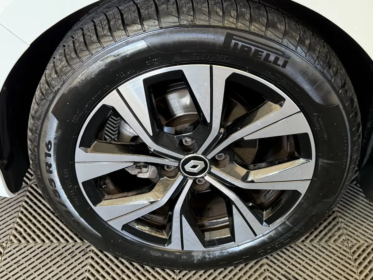 Gros plan sur la roue avant droite d'une Renault Clio blanche avec jante alliage bicolore et pneu Pirelli.