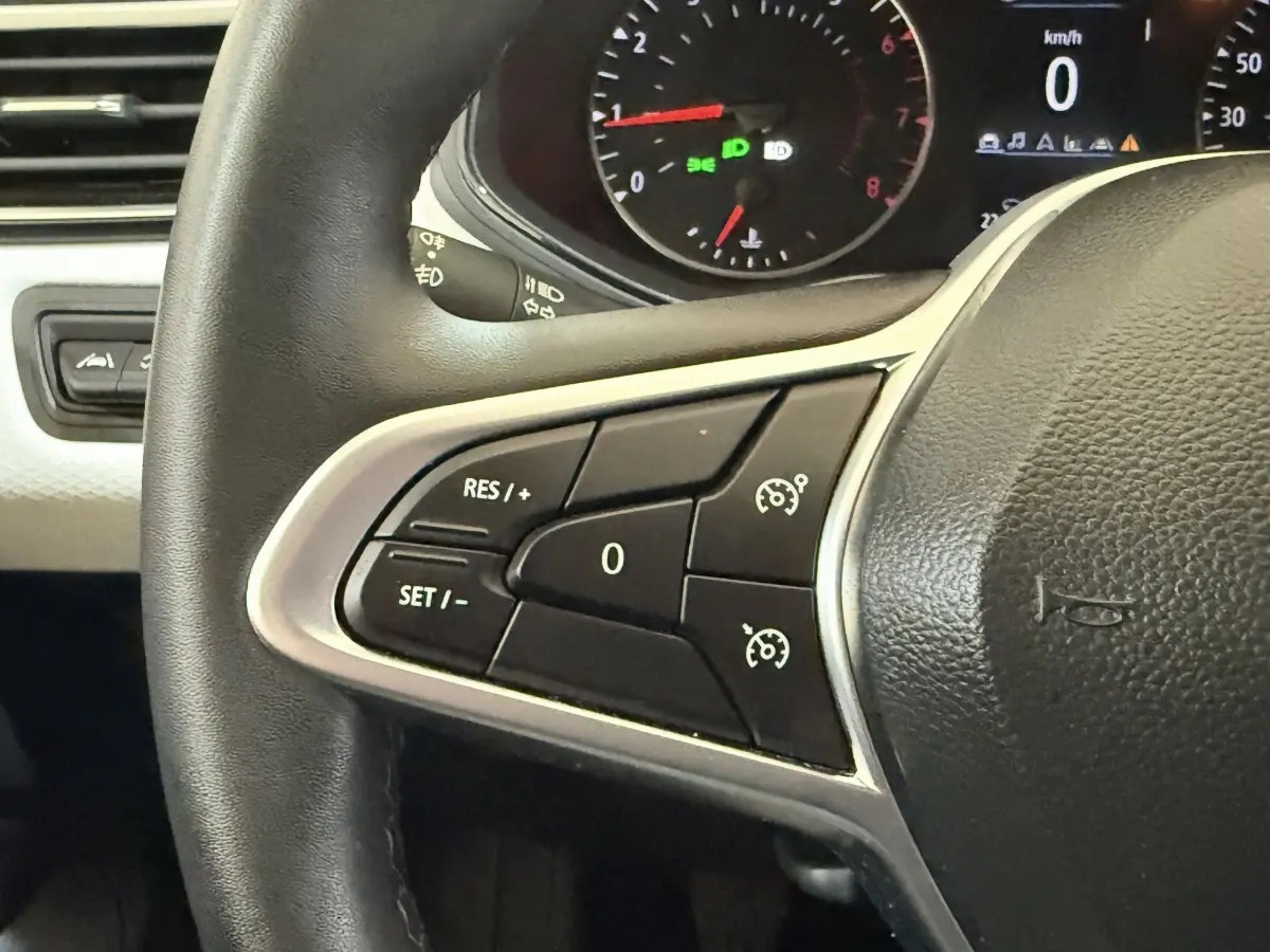 Gros plan sur le volant noir de la Renault Clio 2023 avec commandes du régulateur de vitesse et tableau de bord partiel.