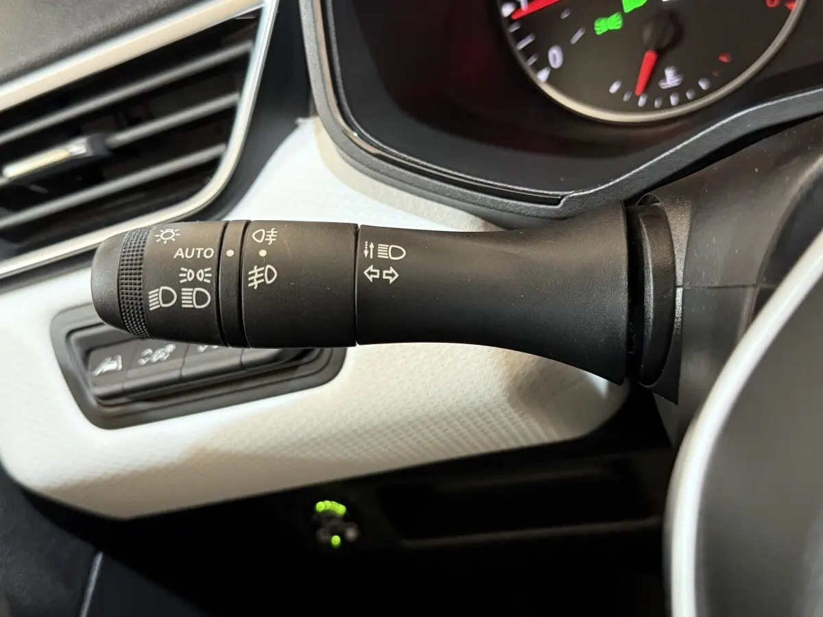 Gros plan sur la commande des phares et clignotants à gauche du volant, tableau de bord blanc texturé en arrière-plan.