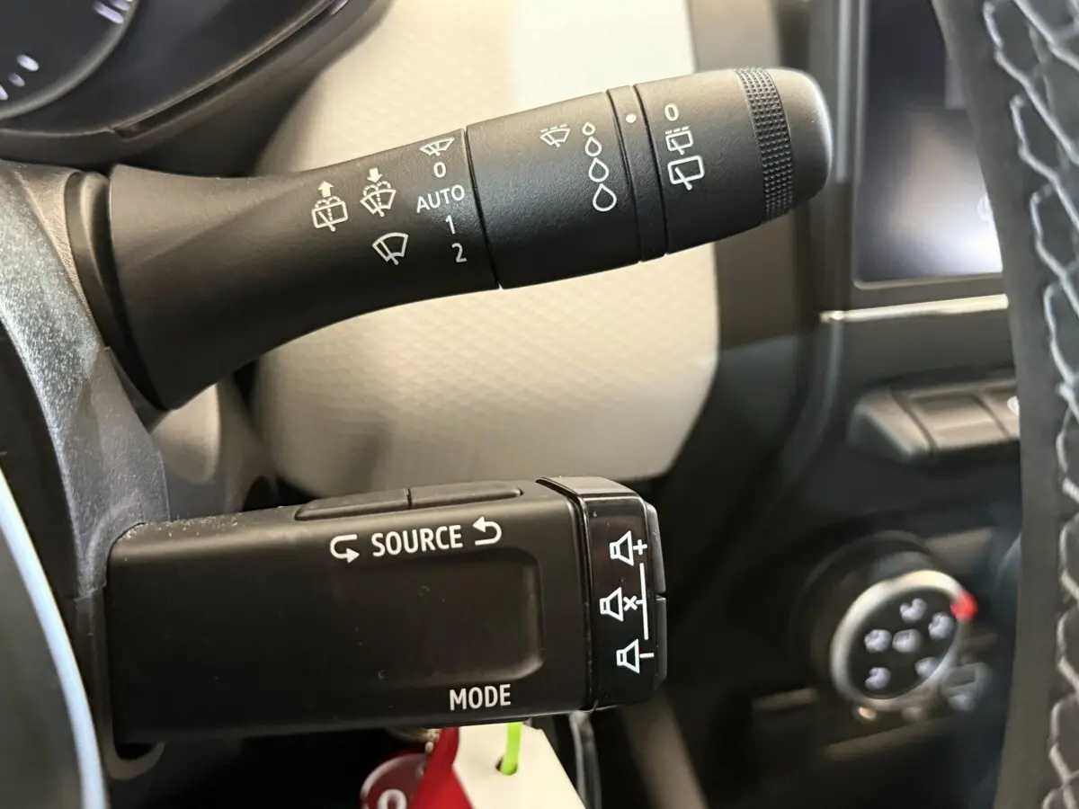 Gros plan sur les commandes au volant noir de la Renault Clio Business TCe 100 GPL, avec tableau de bord partiellement visible.