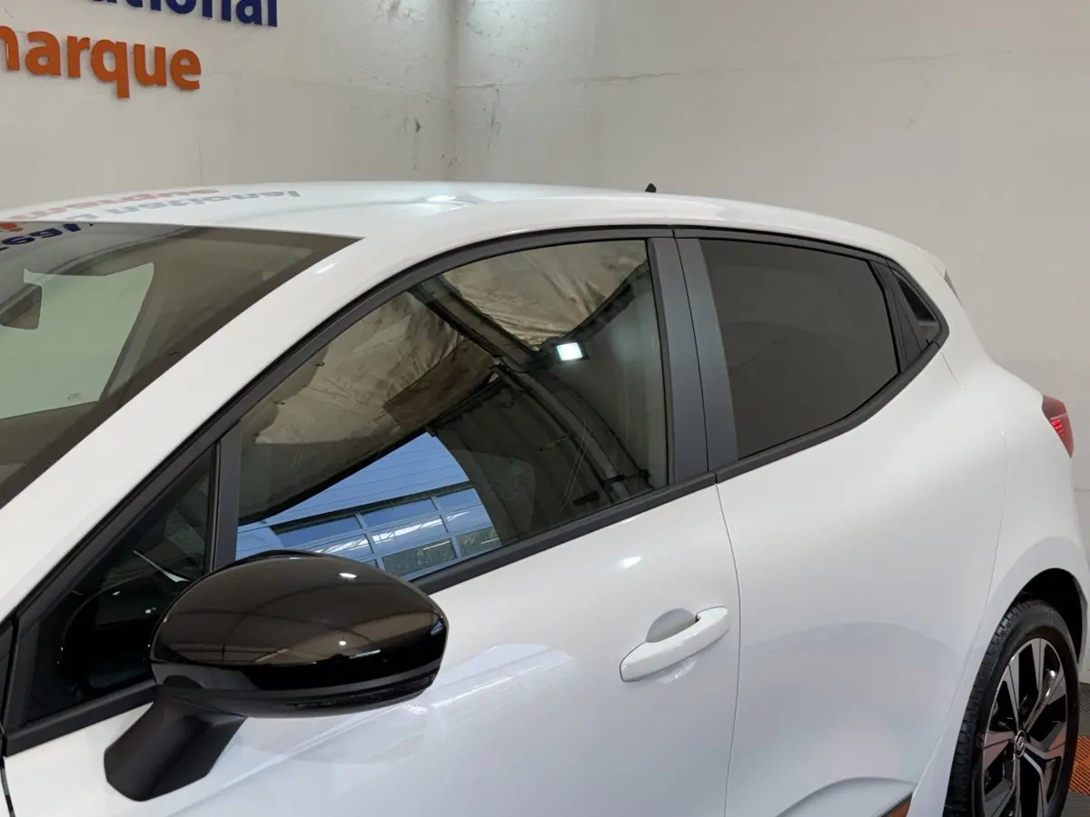 Vue de profil côté gauche sur une Renault Clio Business blanche avec rétroviseur noir et vitres teintées.