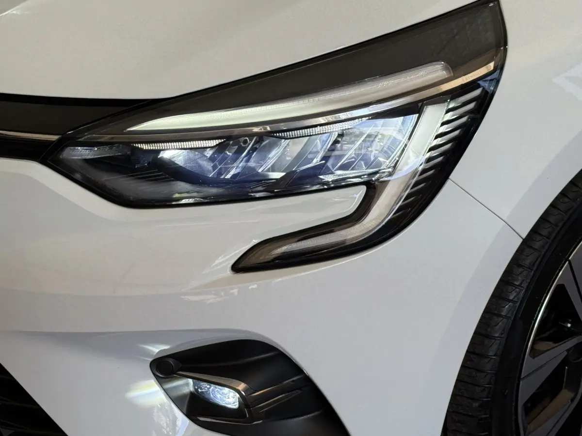 Gros plan sur le phare avant droit blanc de la Renault Clio Business TCe 100 GPL 2023 avec feu LED et partie de la roue visible.
