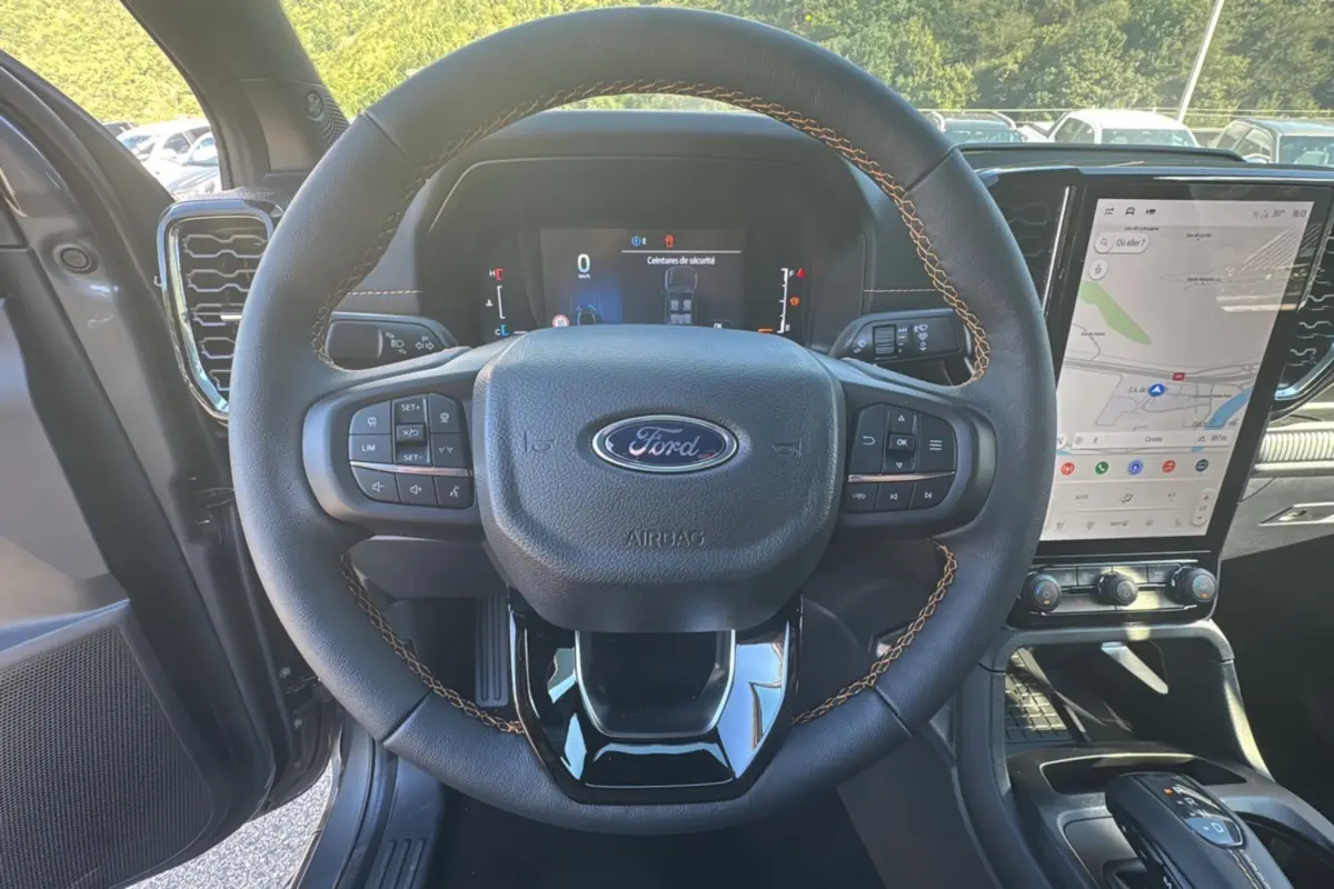 Vue intérieure centrée sur le volant cuir noir avec surpiqûres marron du Ford Ranger 2025, écran tactile et tableau de bord visibles.