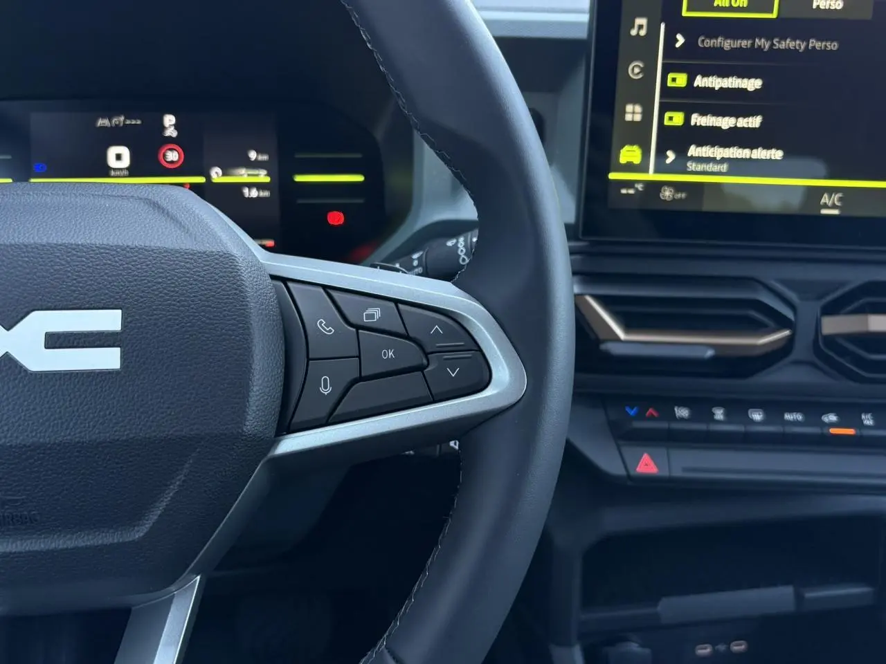 Vue rapprochée du volant et tableau de bord digital du Dacia Duster 2026, avec commandes au volant et écran tactile.